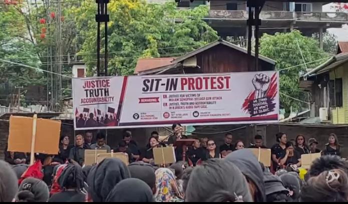Stage and banner displayed during a protest rally demanding justice and accountability in Manipur.