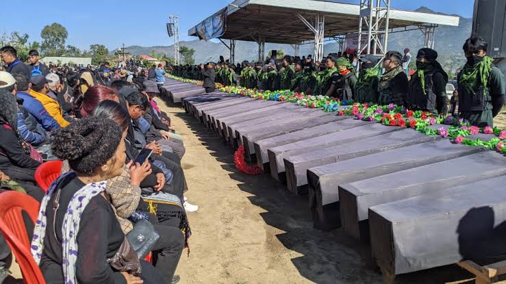 rows of symbolic coffins placed at a memorial gathering with people paying respects