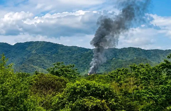 Black smoke rising above forested hills following a reported village fire