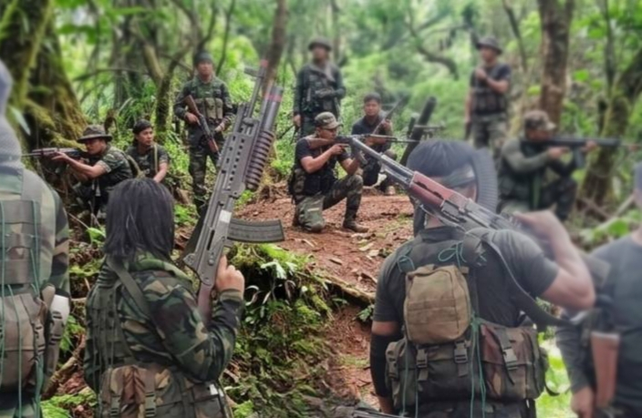 group of armed men in camouflage uniforms in forest terrain holding rifles
